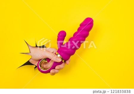 Female hand with magenta vibrator sticking out from yellow paper background. Copy space. 121833838