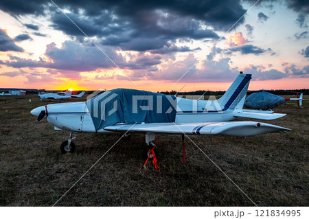 Covered airplanes and helicopters of small aviation at the airfield at picturesque sunrise 121834995