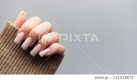 Woman showing stylish pink manicure with brown sleeve on grey background 121838672