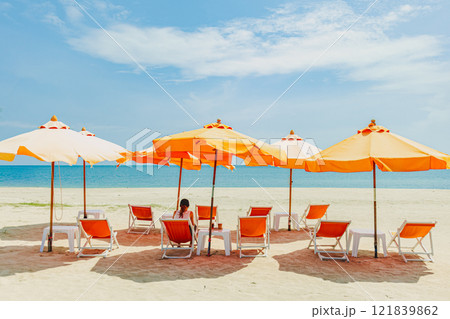Woman sit on the orange umbrella chair set on the beach with blue sky. Woman sit on the orange umbrella chair set on the beach with blue sky. 121839862