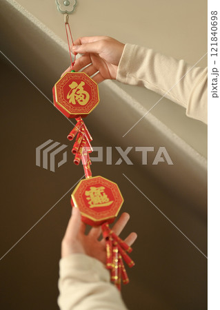 Close up of hands hanging red Chinese New Year decoration adorned with golden Chinese characters for luck and prosperity. Close up of hands hanging red Chinese New Year decoration adorned with golden Chinese characters for luck and prosperity. 121840698