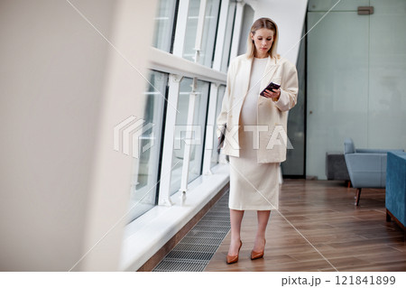Portrait of beautiful pregnant businesswoman confidently working on laptop in a modern business office with a light blue background, wearing a stylish suit and blazer, representing female empowerment Portrait of beautiful pregnant businesswoman confidently working on laptop in a modern business office with a light blue background, wearing a stylish suit and blazer, representing female empowerment 121841899