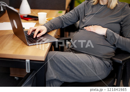 Close up Pregnant woman working on laptop. Cropped pregnant businesswoman typing on laptop while sitting at her working place in office 121841985