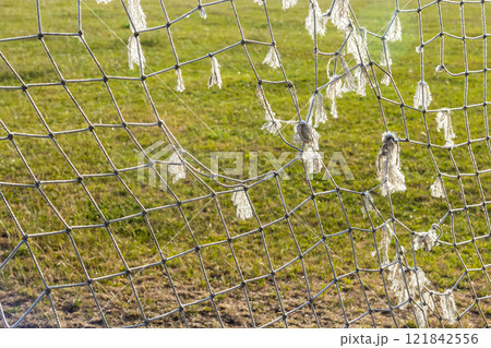Torn soccer net reveals signs of wear at local sports field during afternoon sunlight Torn soccer net reveals signs of wear at local sports field during afternoon sunlight 121842556