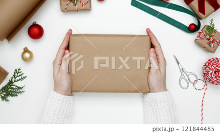 Cozy holiday setting, womans hands wrapping Christmas gifts with festive decorations 121844485