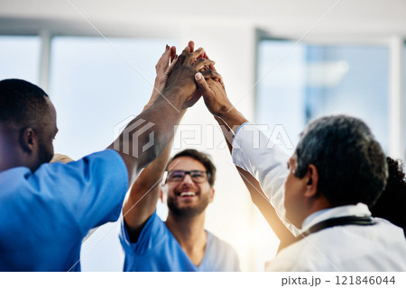 Doctors celebrating medical success after working together as a team and give each other motivating a high five as a group in a hospital. Healthcare workers joining hands in a huddle showing teamwork 121846044