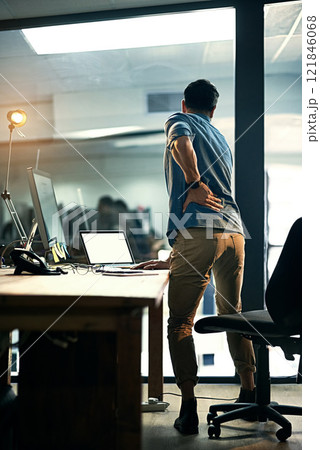 Putting his health at risk for the sake of business. Rearview shot of a businessman suffering from backache while working at night. 121846068