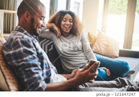 Happy, laughing and cheerful couple relaxing together and looking at social media on a phone at home while sitting on the sofa inside. Young husband and wife enjoying browsing online on a sunny day Happy, laughing and cheerful couple relaxing together and looking at social media on a phone at home while sitting on the sofa inside. Young husband and wife enjoying browsing online on a sunny day 121847247