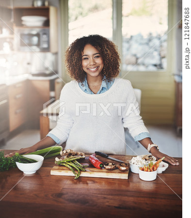 Portrait of happy black woman preparing healthy food in a kitchen at home. Young African American using fresh vegetables to make a delicious, balanced low carb meal. Lady on a cleanse and detox diet Portrait of happy black woman preparing healthy food in a kitchen at home. Young African American using fresh vegetables to make a delicious, balanced low carb meal. Lady on a cleanse and detox diet 121847688