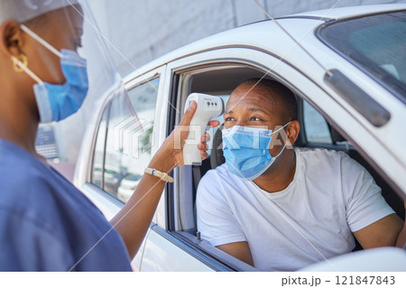 Drive thru for covid screening or testing service for people driving or traveling. Black man wearing a mask in a car getting his temperature test using an infrared thermometer as coronavirus protocol 121847843