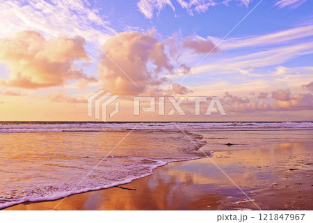 Beautiful beach and fresh ocean against a soft cloudy sky at sunset with copy space. Waves washing onto a shore on a relaxing, scenic coast. Golden sun shining on fluffy clouds on a fresh morning 121847967
