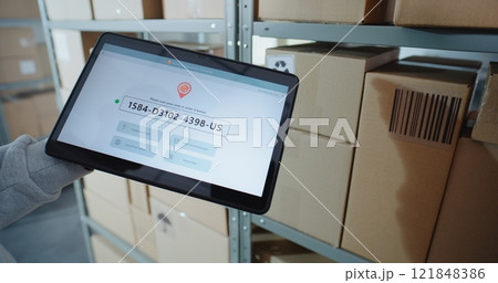 Postal Warehouse Associate Scans Code on Cardboard Box, Checks Parcel Information on Tablet 121848386