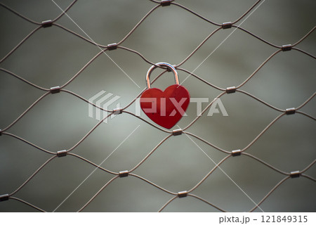 Closeup of red padlock in shaped heart on metallic fence in border water Closeup of red padlock in shaped heart on metallic fence in border water 121849315