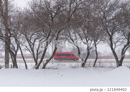 【ウクライナ】東部ドンバス地方の積雪と街路樹と道をを走る赤いバン 【ウクライナ】東部ドンバス地方の積雪と街路樹と道をを走る赤いバン 121849402
