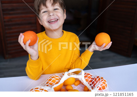 A child with a joyful smile holds an orange and a mandarin, looking at the camera. A child with a joyful smile holds an orange and a mandarin, looking at the camera. 121851165