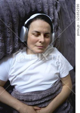 a senior woman wearing sonic hues sleep headphones sleeping under a weighted blanket 121852590