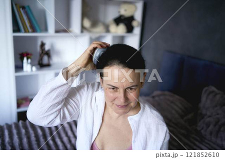 a senior woman massages her head with an electric head and neck massager to stimulate hair growth a senior woman massages her head with an electric head and neck massager to stimulate hair growth 121852610