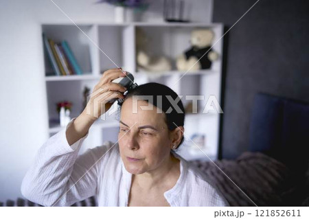 a senior woman massages her head with an electric head and neck massager to stimulate hair growth a senior woman massages her head with an electric head and neck massager to stimulate hair growth 121852611
