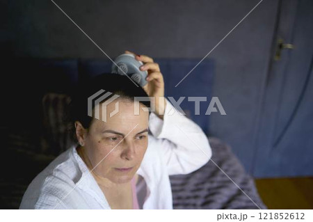 a senior woman massages her head with an electric head and neck massager to stimulate hair growth a senior woman massages her head with an electric head and neck massager to stimulate hair growth 121852612