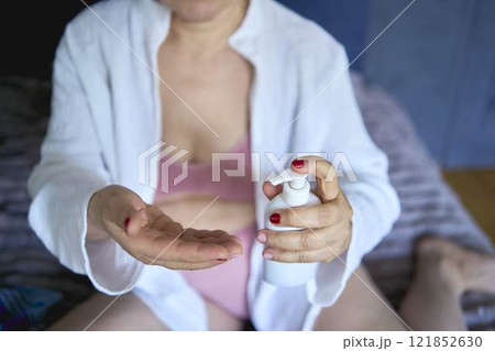 a senior woman in underwear on the bed performs routine self-care with face and body cosmetics a senior woman in underwear on the bed performs routine self-care with face and body cosmetics 121852630
