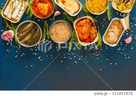 Different open tin cans with canned fish like salmon, mackerel, sprat, sardine, tuna, and herring, among spices and herbs on a blue background, viewed from the top Different open tin cans with canned fish like salmon, mackerel, sprat, sardine, tuna, and herring, among spices and herbs on a blue background, viewed from the top 121853878