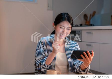 夜に家でスマホでスポーツ観戦をする若い女性 夜に家でスマホでスポーツ観戦をする若い女性 121854899