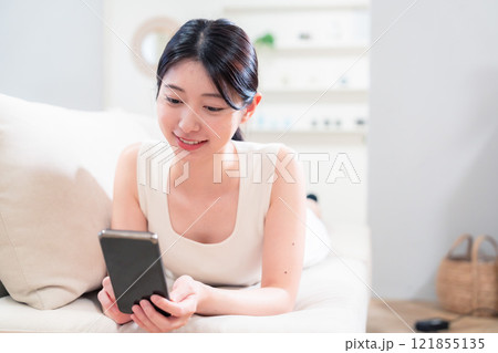 ソファで寝転がってスマホを使う若い女性 ソファで寝転がってスマホを使う若い女性 121855135