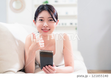 ソファで寝転がってスマホを使う若い女性 121855140