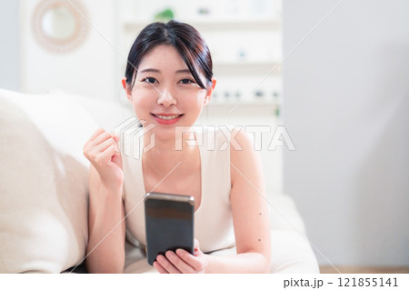 ソファで寝転がってスマホを使う若い女性 121855141