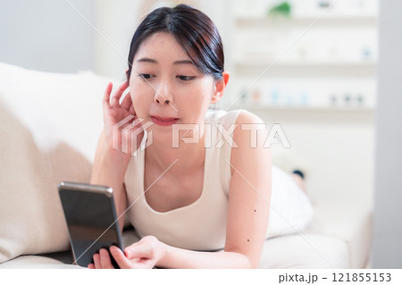 ソファで寝転がってスマホを使う若い女性 121855153