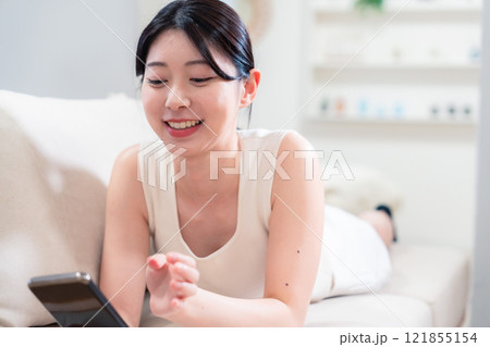 ソファで寝転がってスマホを使う若い女性 121855154
