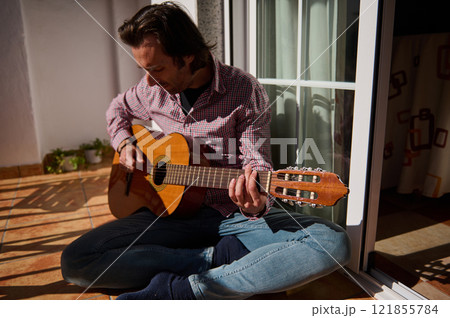 Man playing acoustic guitar while sitting on a sunny home patio 121855784