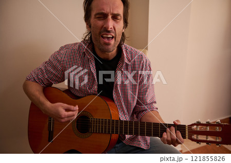 Man passionately playing a classical guitar while singing indoors Man passionately playing a classical guitar while singing indoors 121855826