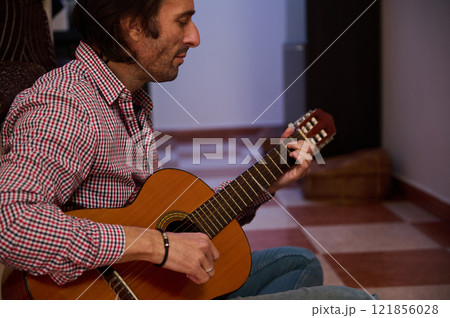 Man playing classical guitar indoors creating a relaxing and musical ambiance Man playing classical guitar indoors creating a relaxing and musical ambiance 121856028