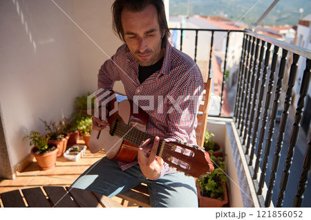 Man playing an acoustic guitar on a bright outdoor terrace Man playing an acoustic guitar on a bright outdoor terrace 121856052