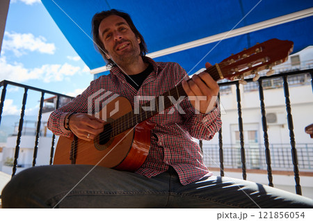 Man playing acoustic guitar outdoors on a sunny day with a blue canopy Man playing acoustic guitar outdoors on a sunny day with a blue canopy 121856054