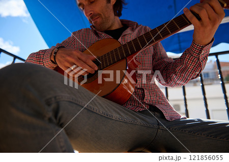 Man playing acoustic guitar outdoors under a blue sky and umbrella shade Man playing acoustic guitar outdoors under a blue sky and umbrella shade 121856055