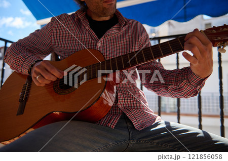 Man playing an acoustic guitar on a sunny day outside on a balcony Man playing an acoustic guitar on a sunny day outside on a balcony 121856058