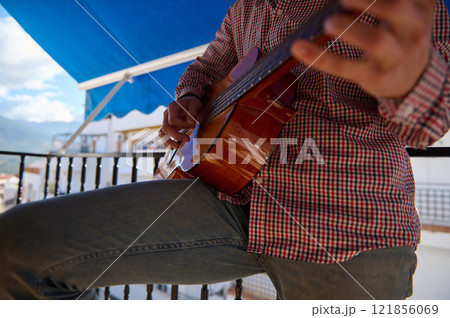 Close-up of a person playing a guitar outdoors on a sunny balcony 121856069