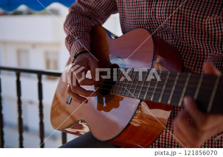 Close-up of a guitarist playing an acoustic guitar on a balcony 121856070