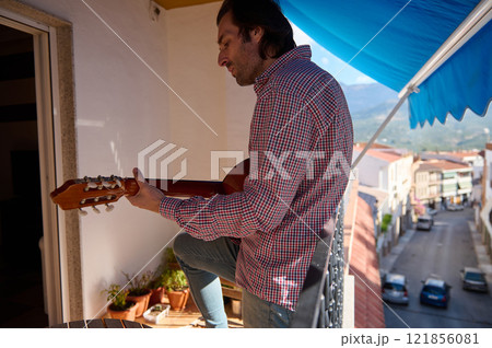 Man playing a guitar on a sunny balcony with a relaxing view Man playing a guitar on a sunny balcony with a relaxing view 121856081