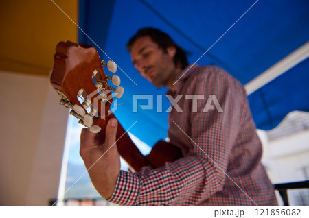 Musician Playing Acoustic Guitar Under Outdoor Shade on a Sunny Day 121856082