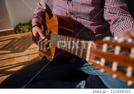 Close-up view of acoustic guitar being played in a cozy outdoor setting 121856103