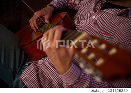 Close-up of a person playing an acoustic guitar indoors 121856289