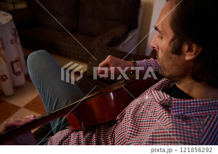Man playing an acoustic guitar while relaxing in a cozy home setting 121856292
