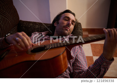 Man relaxing at home while playing an acoustic guitar in leisure time 121856338