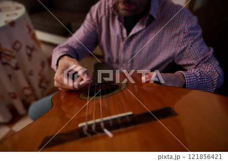 Close-up of a person tuning a classical guitar indoors Close-up of a person tuning a classical guitar indoors 121856421