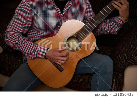 Person Playing Acoustic Guitar Indoors Wearing Checkered Shirt and Blue Jeans Person Playing Acoustic Guitar Indoors Wearing Checkered Shirt and Blue Jeans 121856435