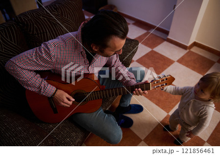 Father Playing Guitar for Toddler in Cozy Home Interior Setting Father Playing Guitar for Toddler in Cozy Home Interior Setting 121856461