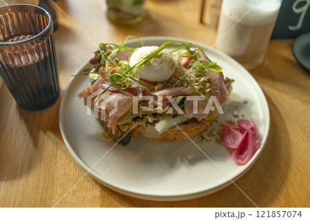 Toast sandwich with gouda cheese and turkey ham filled with tomato and lettuce on a bright background with ingredients in blurry background. Served with coffee and orange juice and eggs 121857074